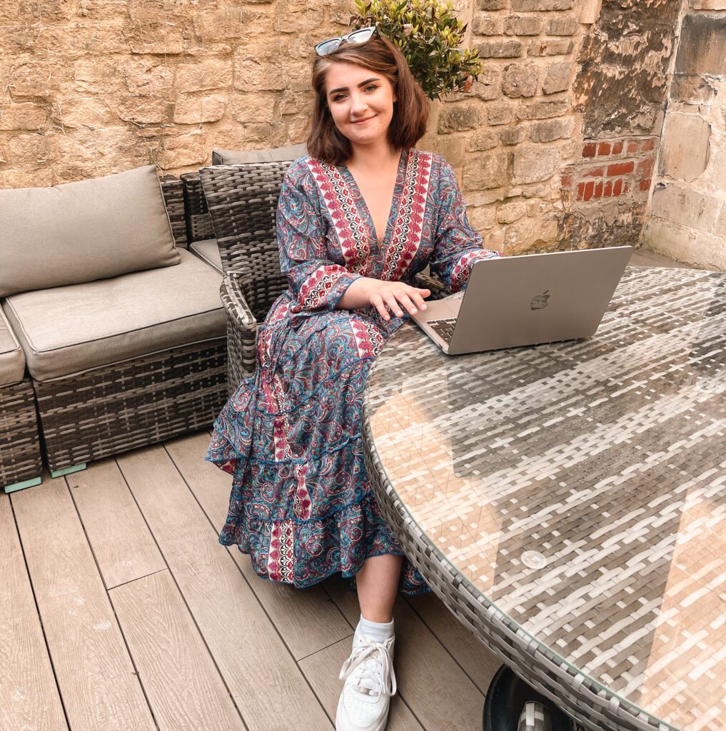 Local Bath influencer Betsy, sitting at an outdoor co-working space table, working on laptop.